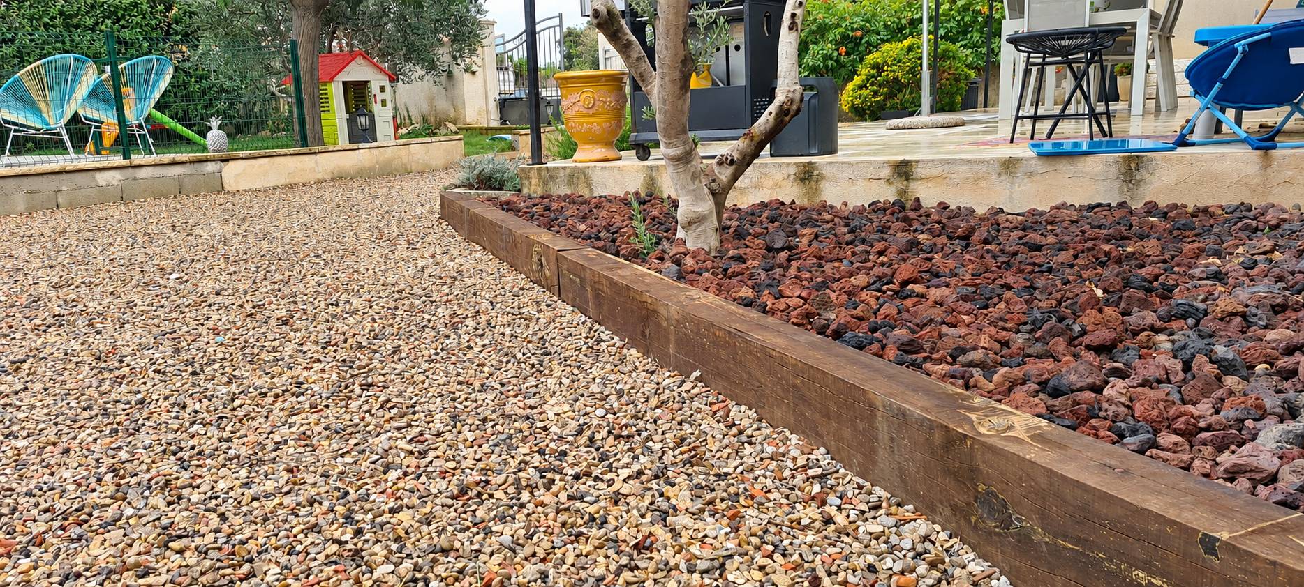 Jardin aménagé avec gravier clair, pouzzolane rouge et bordure en traverse de bois