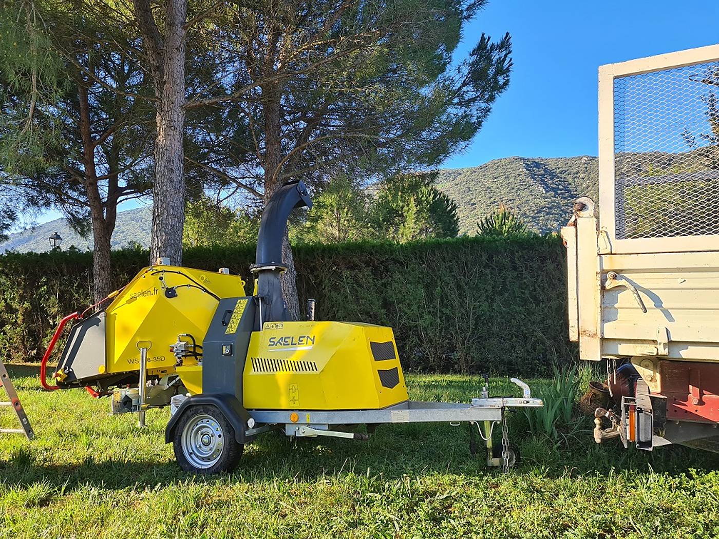 Broyeur de végétaux jaune Saelen sur remorque, dans un jardin arboré