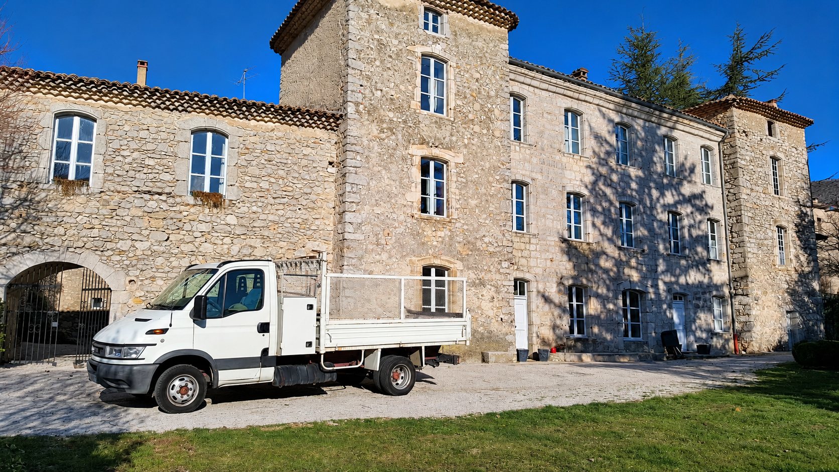 Camion plateau blanc garé devant un grand château en pierre