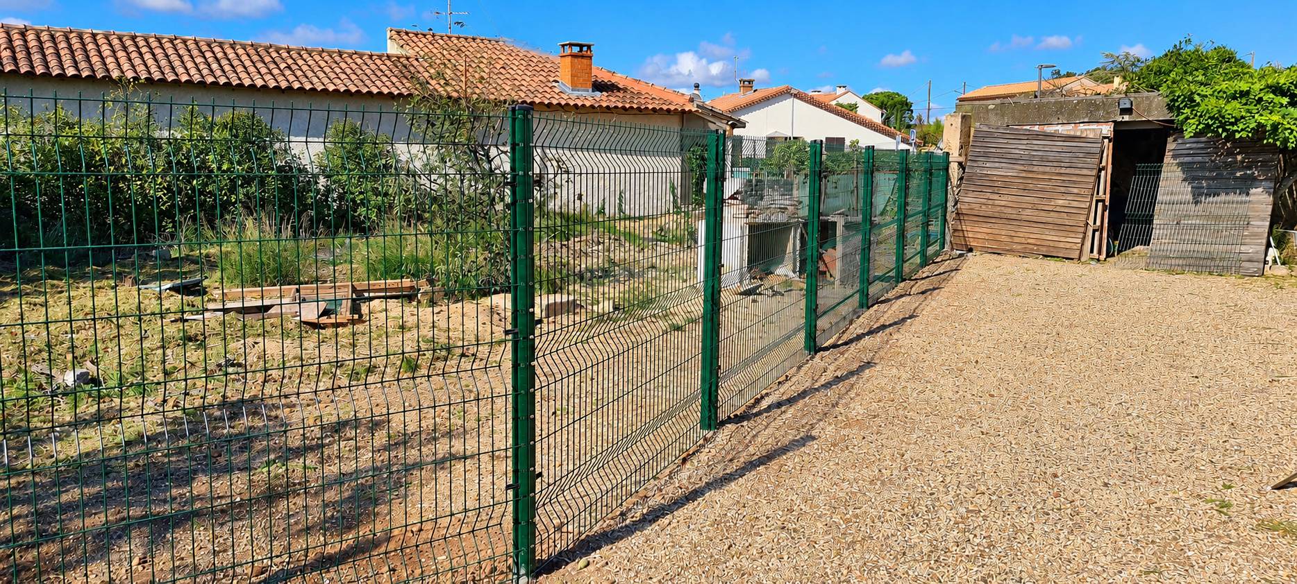 Clôture grillagée verte neuve installée autour d'un terrain près de maisons