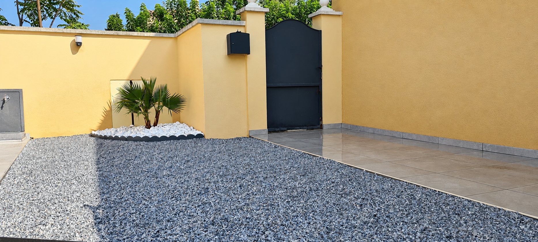 Cour extérieure aménagée avec gravier gris, carrelage et palmier