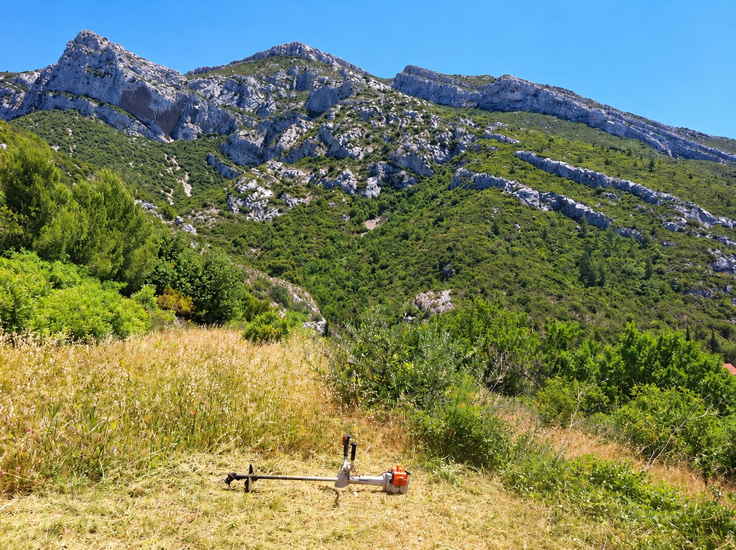 Débroussailleuse posée sur un terrain fauché au pied d'une montagne rocheuse