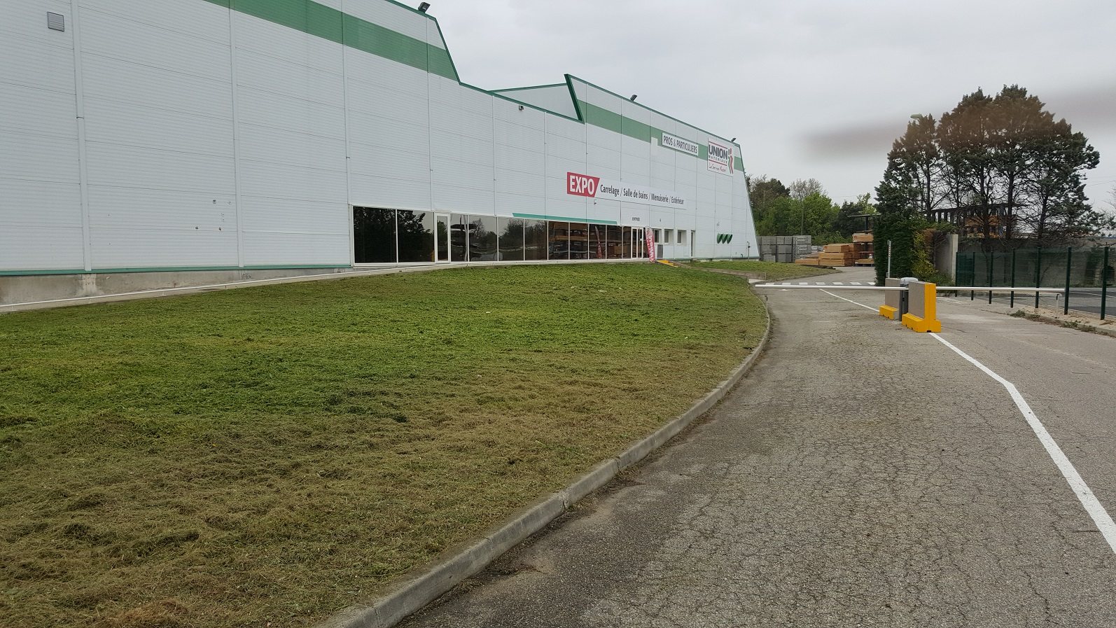 Façade d'un grand magasin de matériaux avec pelouse et barrière d'entrée