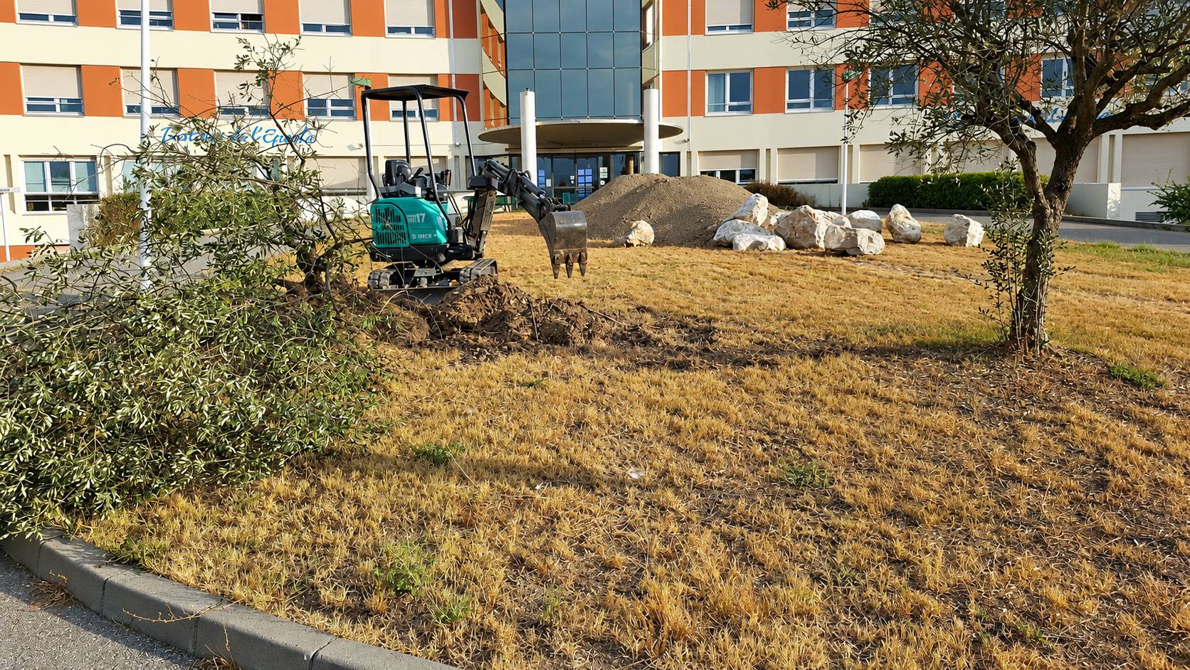 Mini-pelle en travaux de terrassement devant un bâtiment public