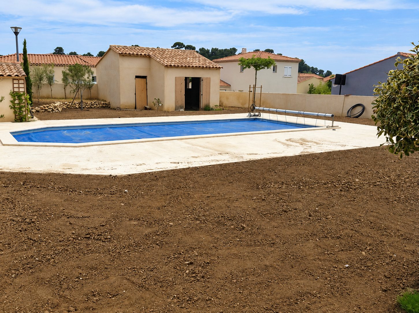 Piscine avec bâche bleue et terrain fraîchement terrassé près d'un pool house