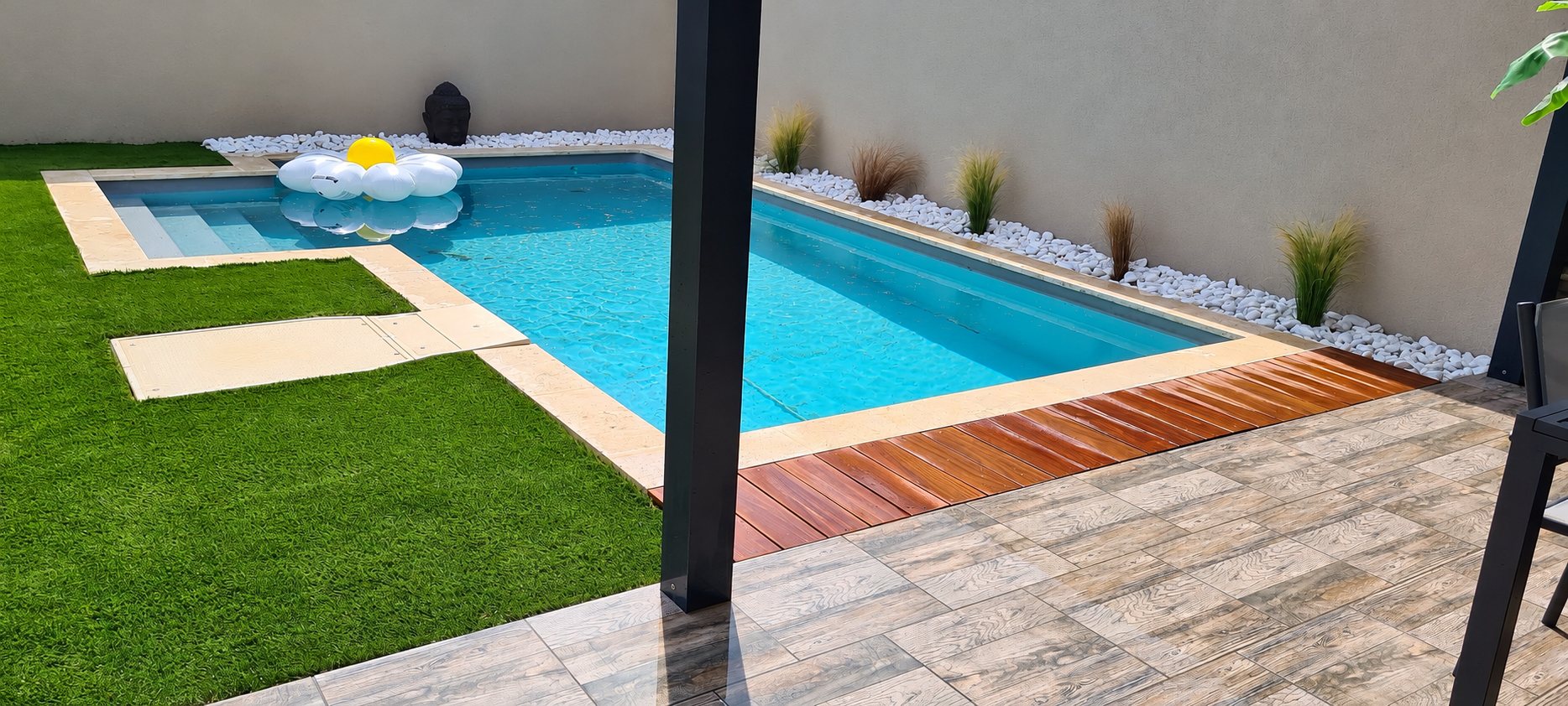 Piscine rectangulaire avec margelles en pierre, pelouse synthétique et terrasse carrelée