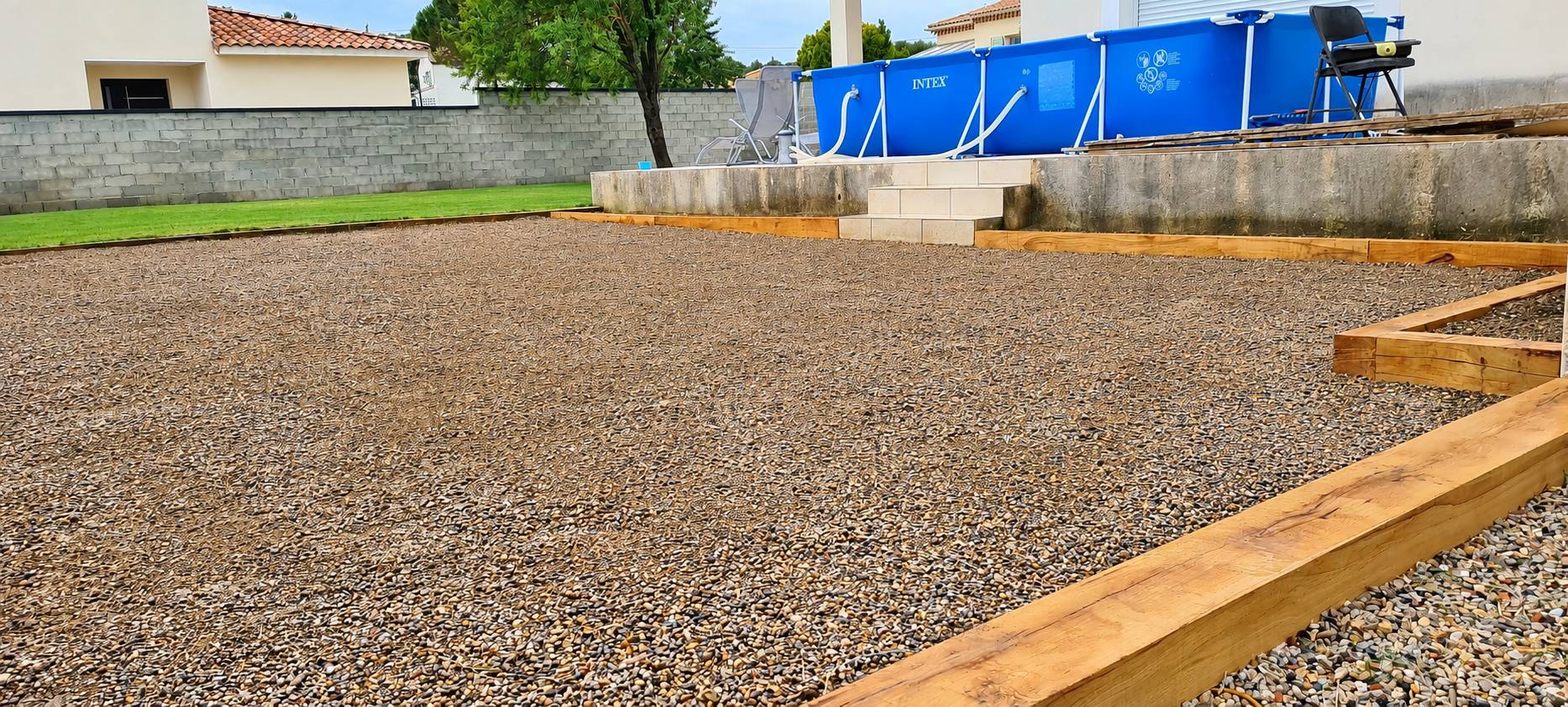 Terrain gravillonné avec bordures en bois près d'une piscine hors-sol